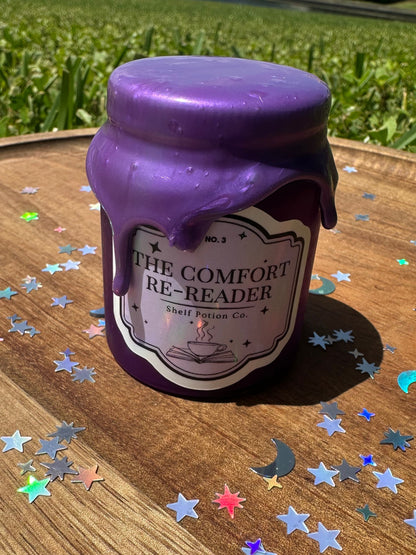 Purple bottle labeled 'The Comfort Re-Reader' on a wooden surface with star-shaped confetti.